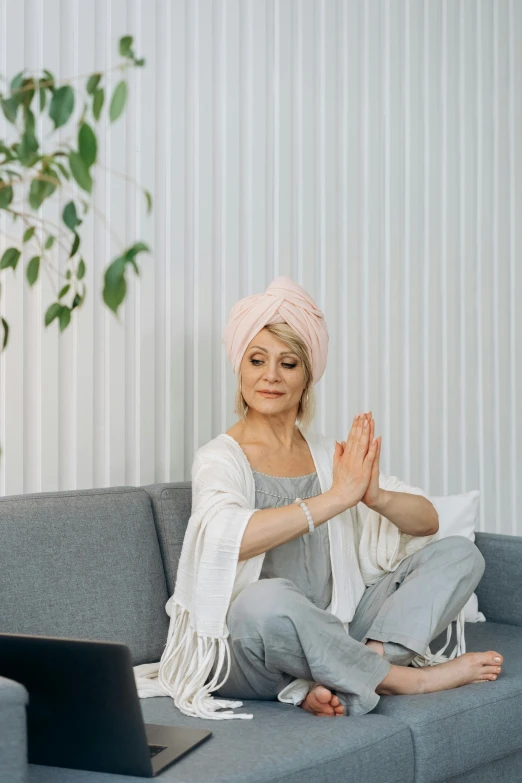 a woman is sitting on a couch in her living room, doing yoga