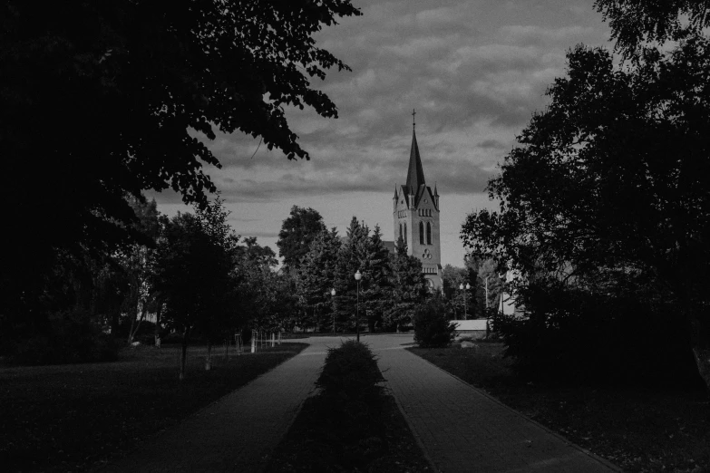 a church tower rises over a dark road surrounded by trees