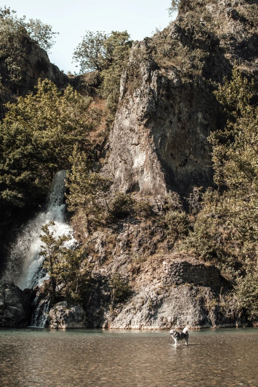 people wading in the water under a very tall waterfall