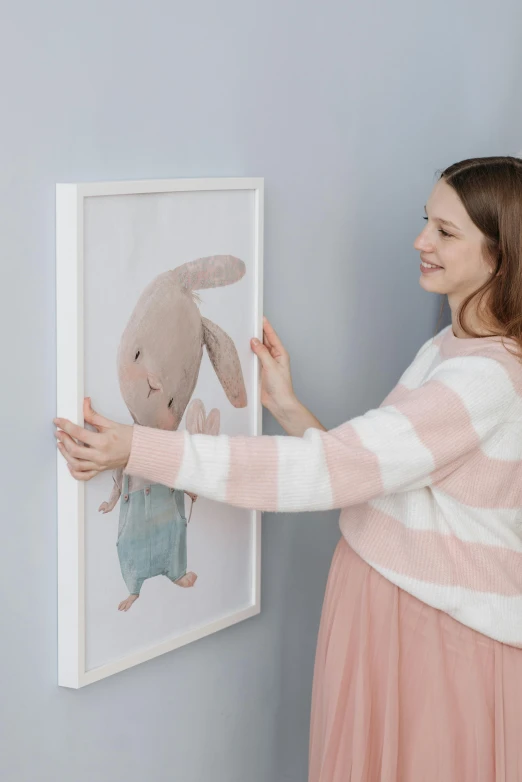 a girl putting a po of a bunny in a frame on the wall