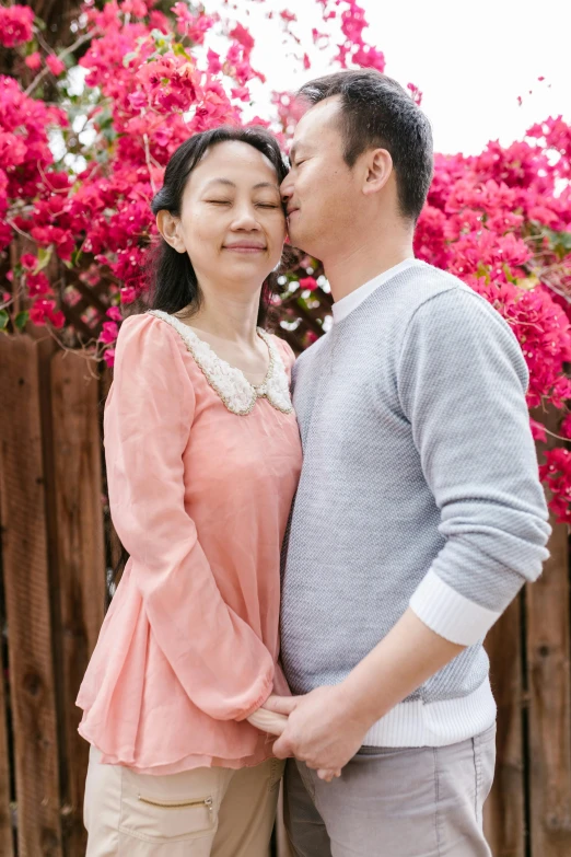 a man and woman kiss each other in front of pink flowers