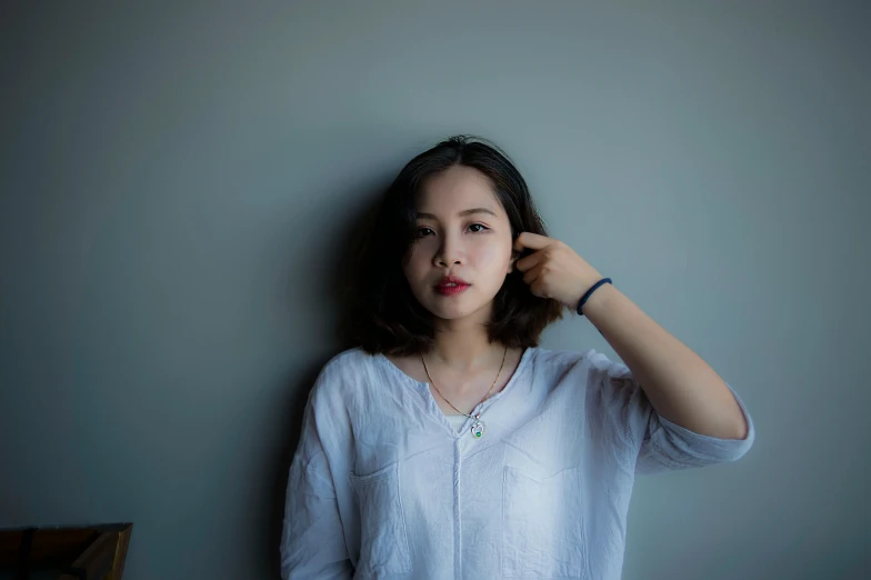 a woman stands next to a wall with her hand over her hair