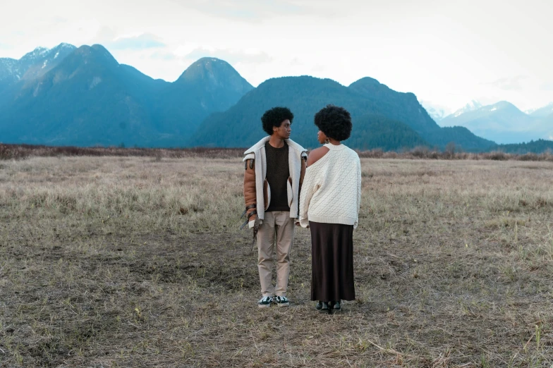 two women stand in an open field looking off into the distance