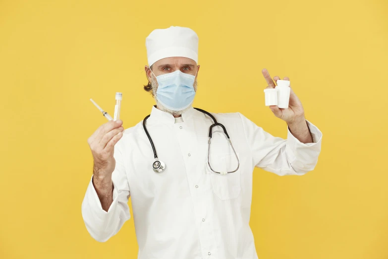 a man in a white uniform and medical mask holds up a v - shape sign while wearing a stethoscope