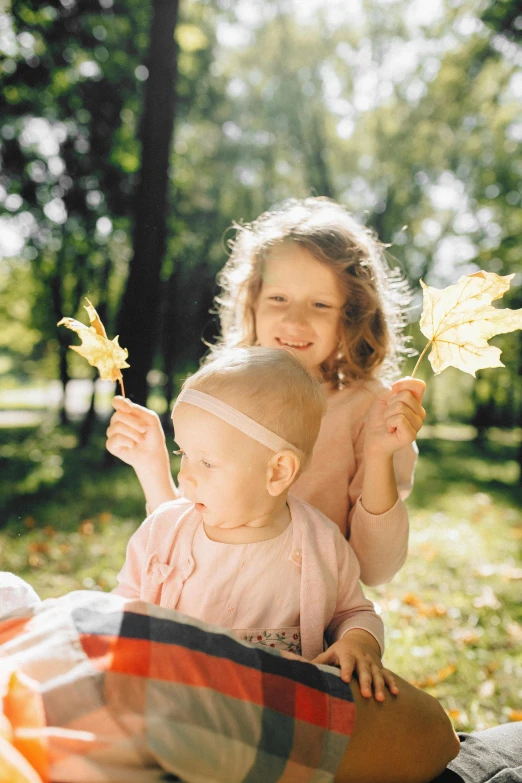 two little girls, one holding a leaf while the other is smiling