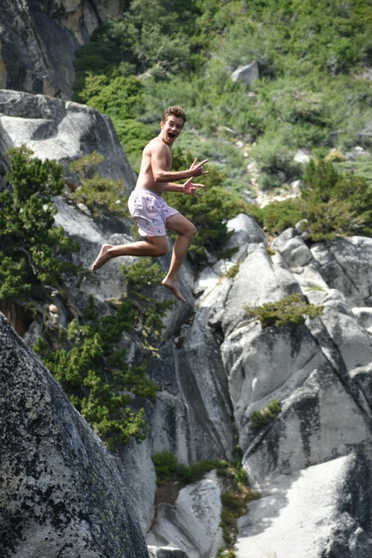 a young man jumping from rock cliff onto the ground