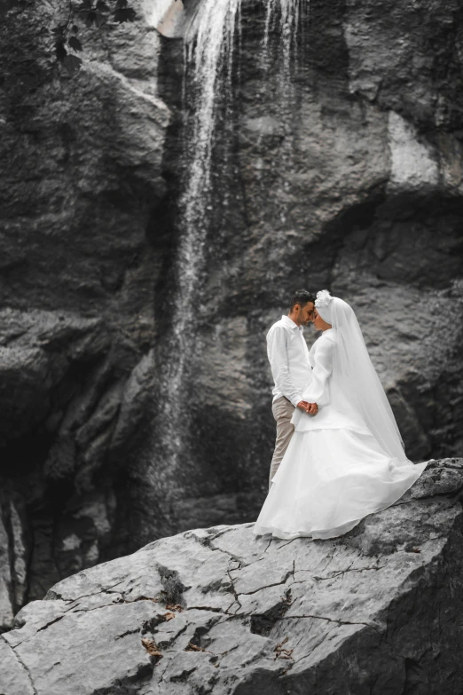 a newly married couple standing in front of a waterfall