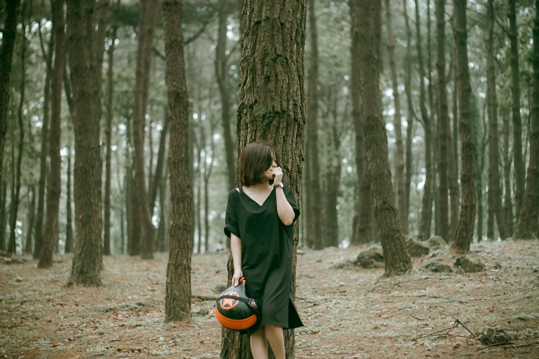 girl in black dress and orange helmet standing on the ground next to tree
