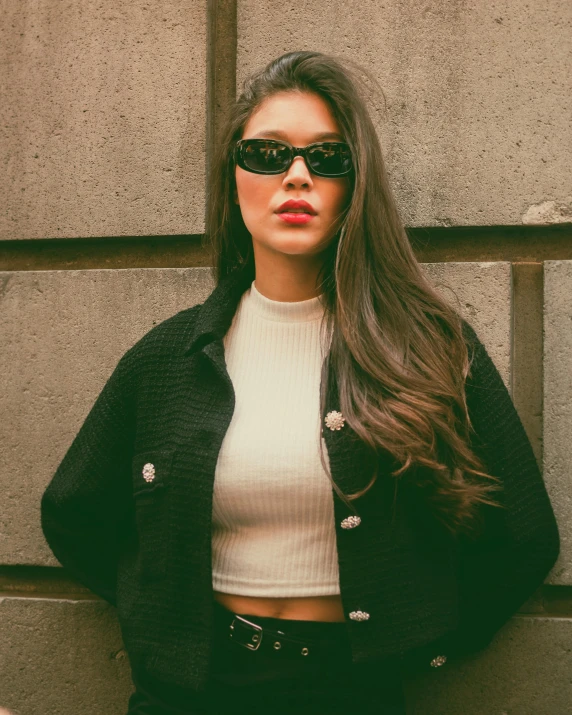 a young woman wearing sunglasses standing against a wall