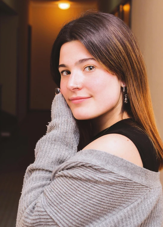 a beautiful young lady in a sweater leaning against the wall