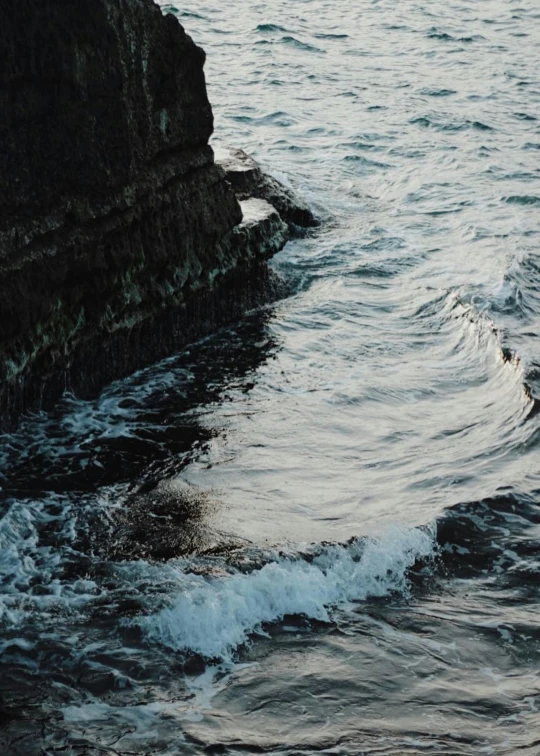 the ocean is gently moving toward an old stone cliff