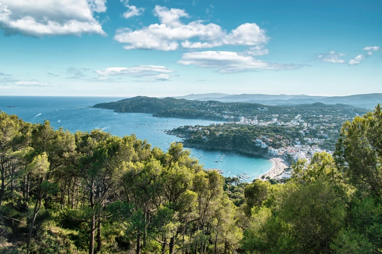 a po from a hill looking out on the blue water and mountains with boats on it