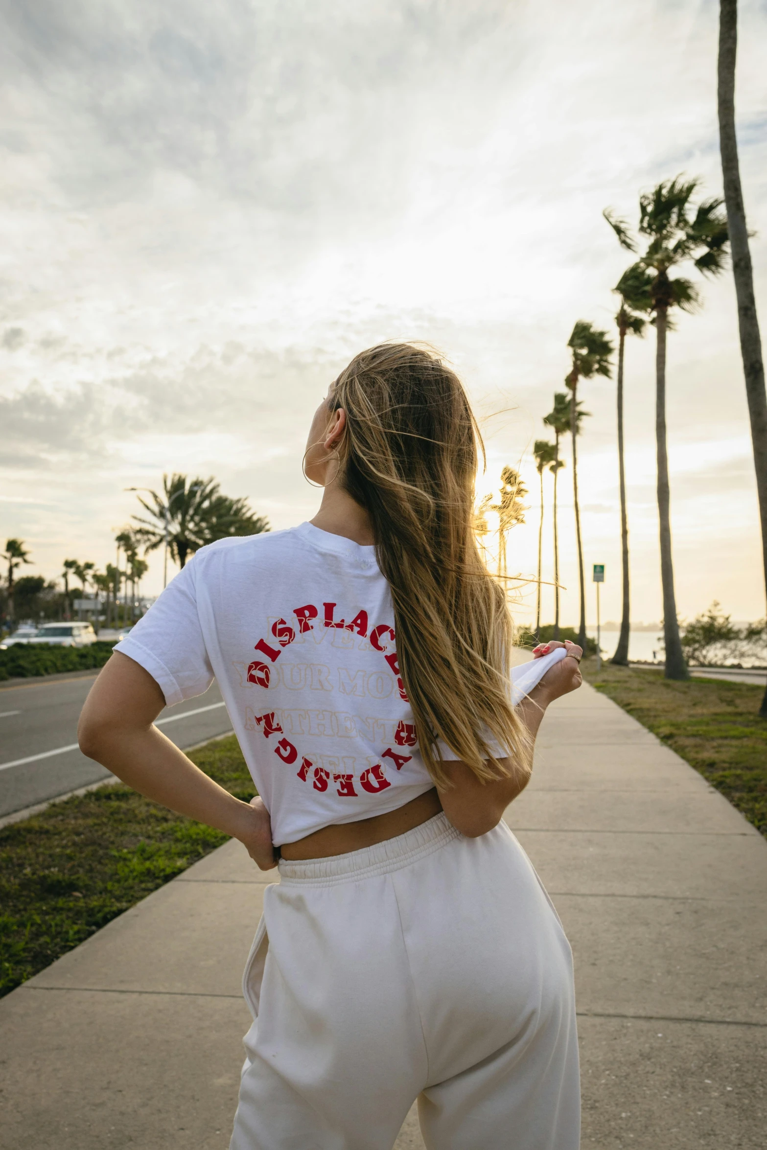 a young woman in a white top stands on a path next to palm trees