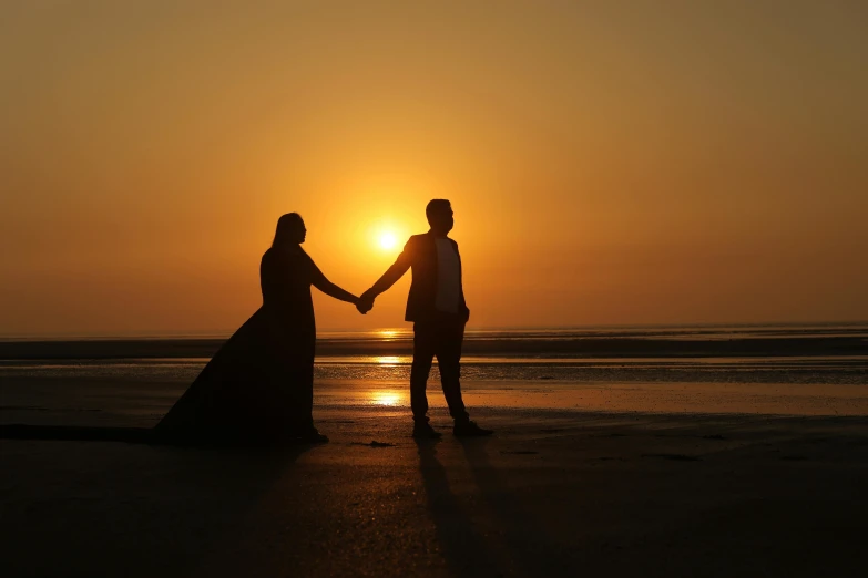 the couple are holding hands and looking at the setting sun