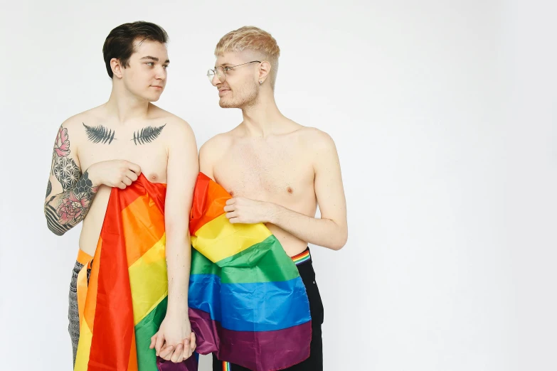 two men are standing side by side one has a rainbow flag on his cape