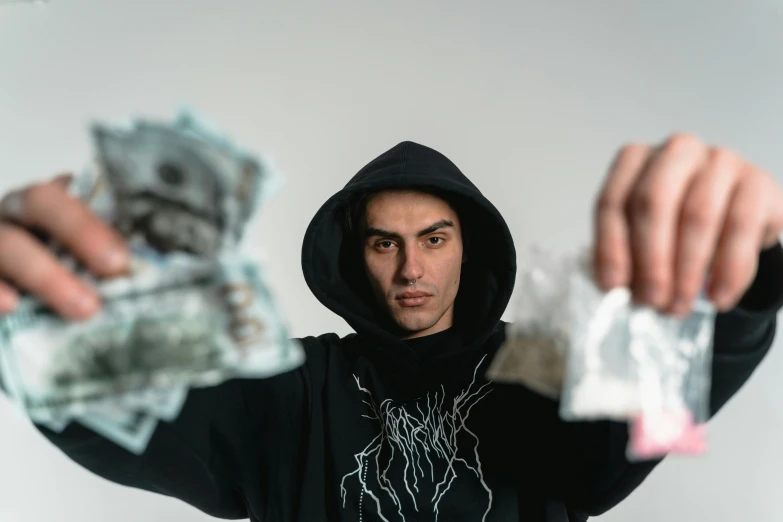 the young man is wearing a hooded jacket and holding out money in both hands
