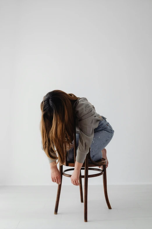 a girl sitting on top of a chair bends over and holds her head