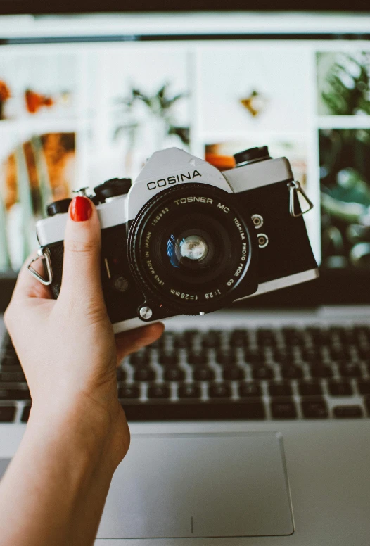 a person holding a camera and looking at a laptop