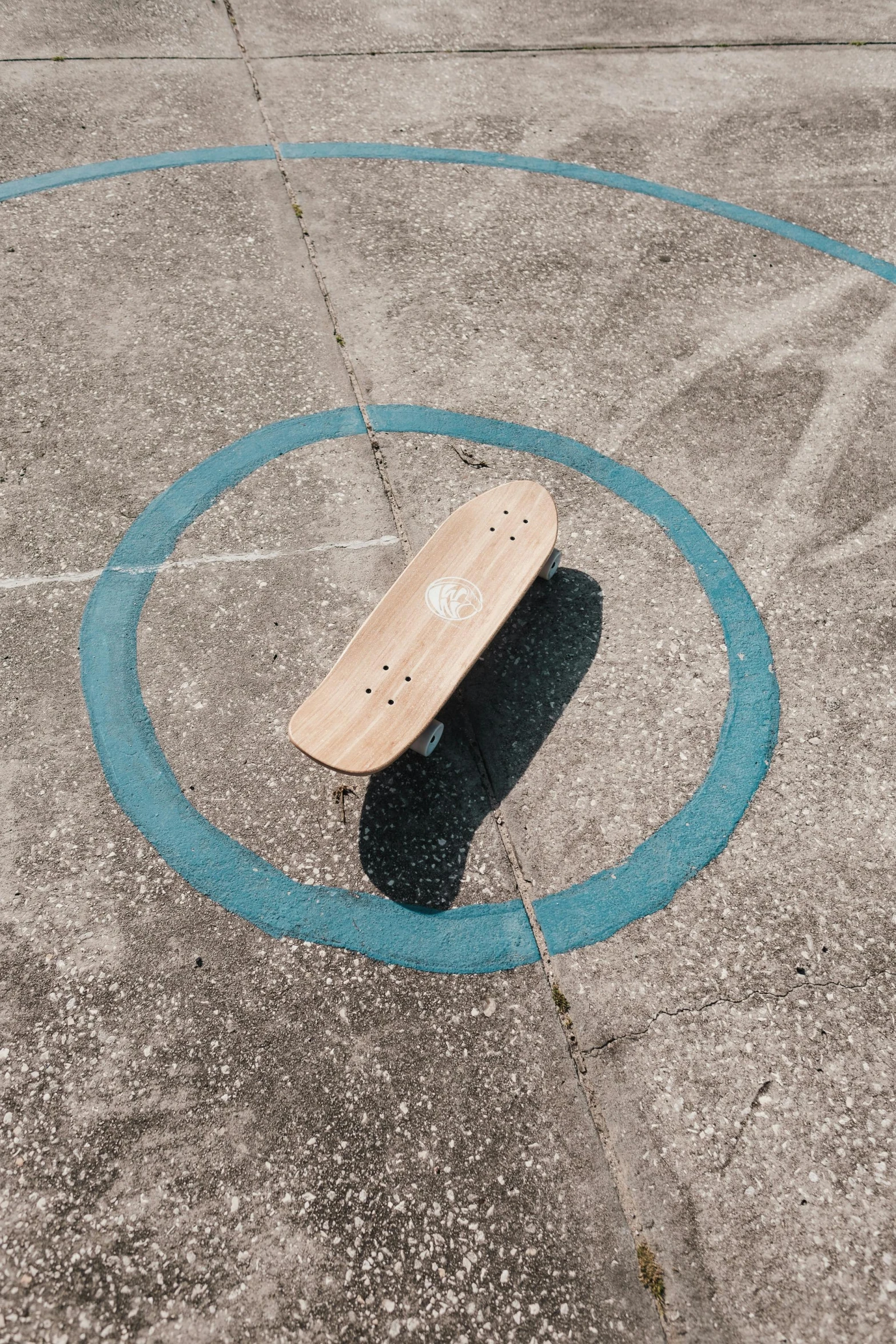 a skateboard sits in a concrete space, with an inner blue circle around it