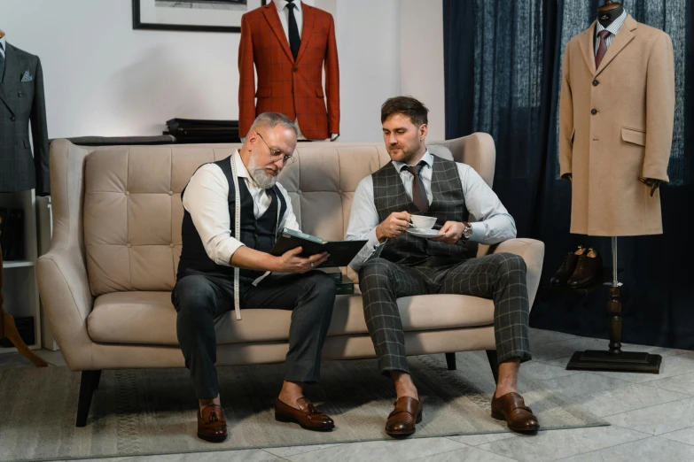 two men sitting on couches next to suits in an office