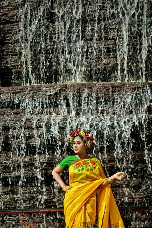 an indian woman stands in front of a waterfall