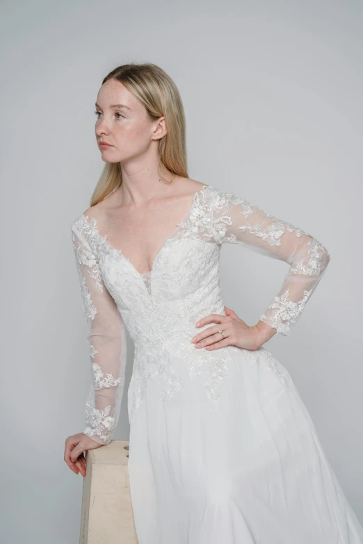 a woman wearing a wedding gown stands against a white background