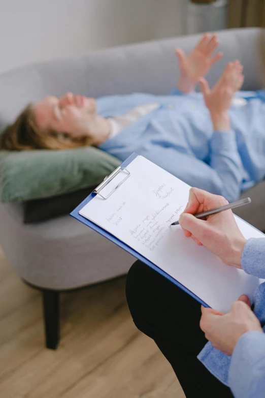 a woman is writing in a notepad while resting on a couch