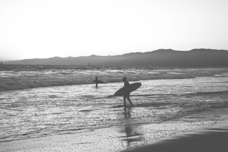 two surfers are running into the ocean with their boards