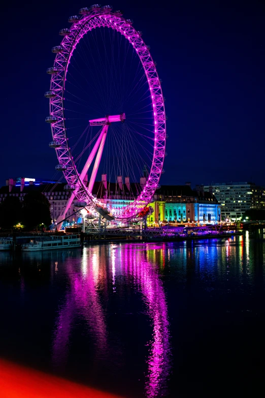 the london eye lit up in pink and purple in the evening