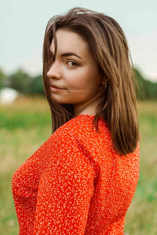 a girl in a red dress poses with grass and trees in the background