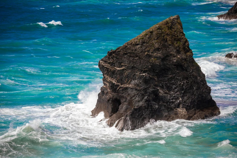 a rock in the ocean and waves crashing on top