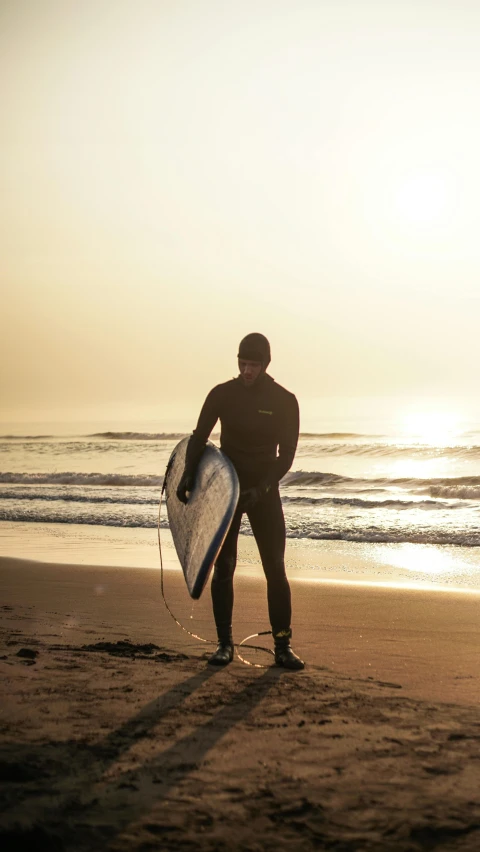 man in a full body wet suit carrying a surf board towards the ocean