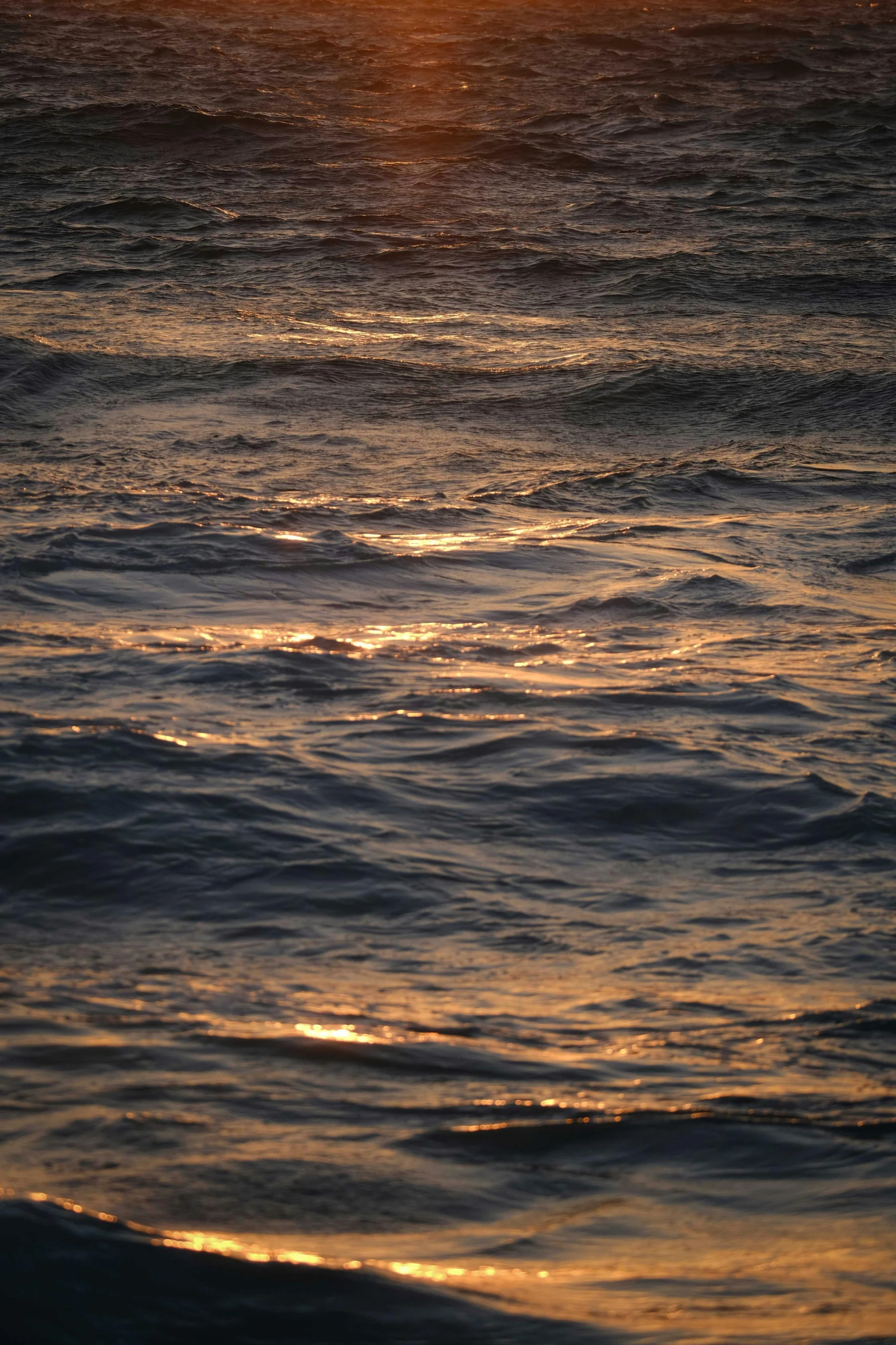 the sun sets on an ocean with the water crashing to shore