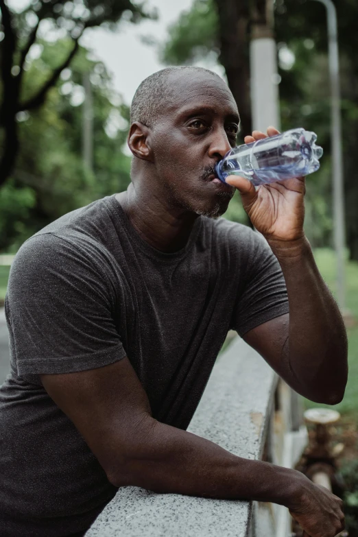 a black man sits on a bench drinking water