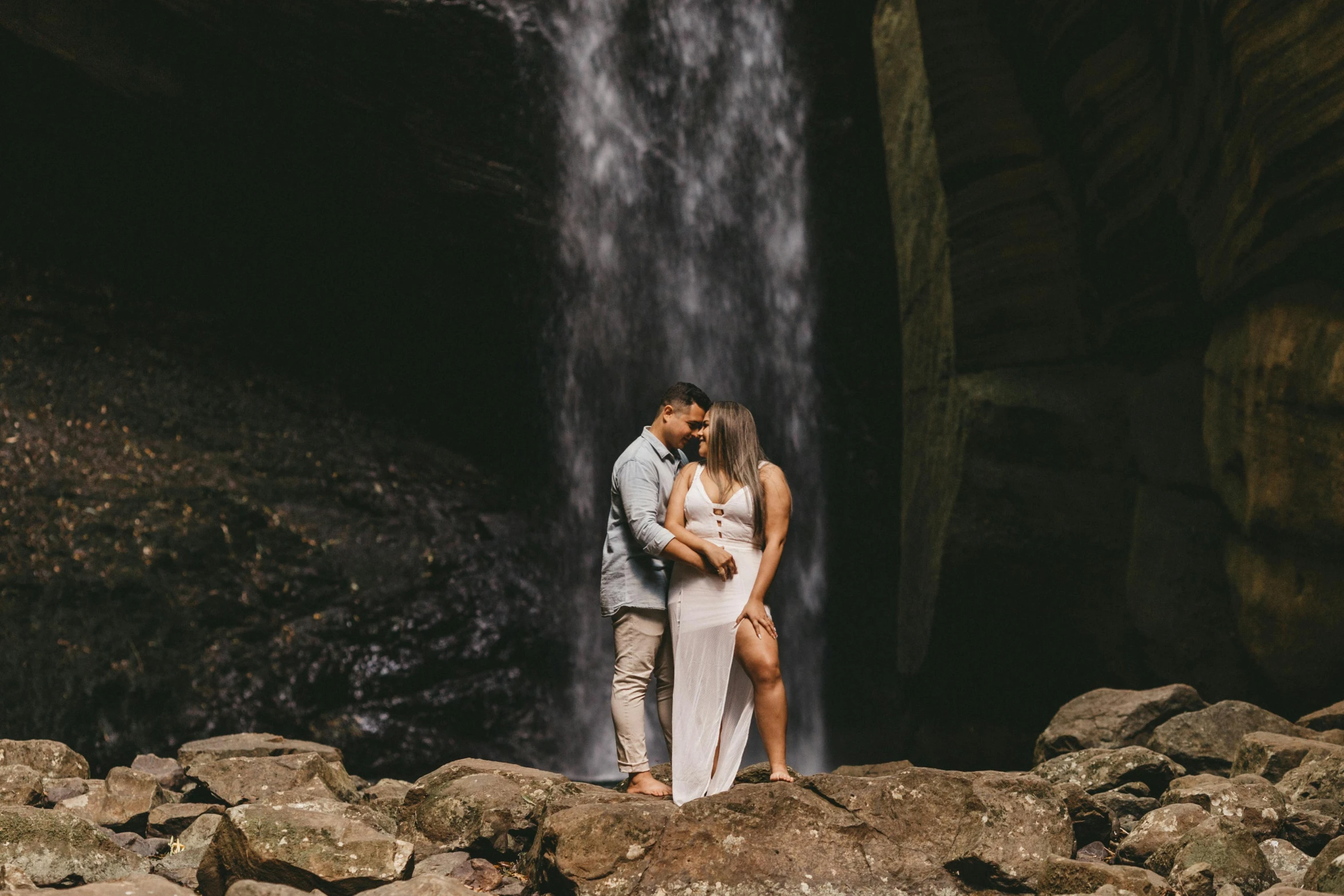 man and woman kissing under waterfall with large rocks