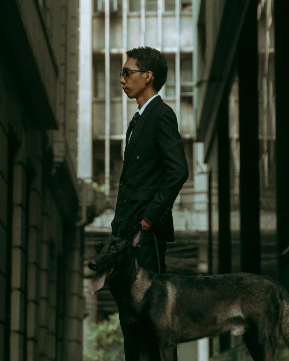 man in suit and glasses standing on street with black dog