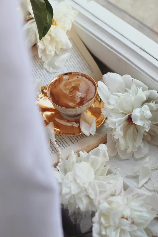 a cup of coffee on a table with a white flower next to it