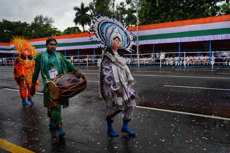 the man is carrying a drum and another in colorful headdress