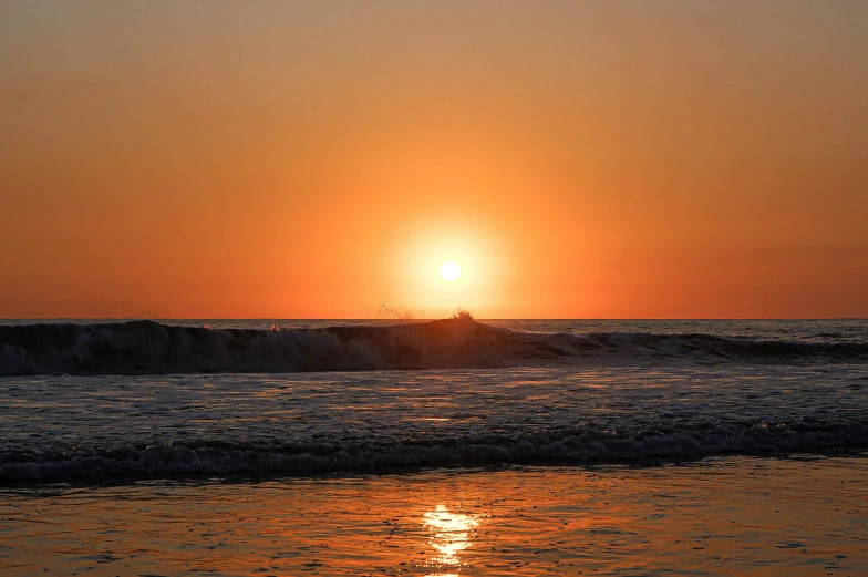 the sun rises over the horizon of an ocean with a surfer