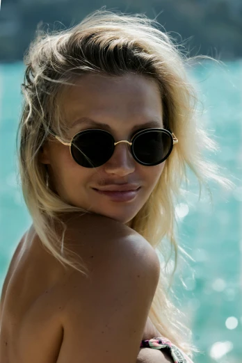 a woman with sunglasses and no top on standing next to the water