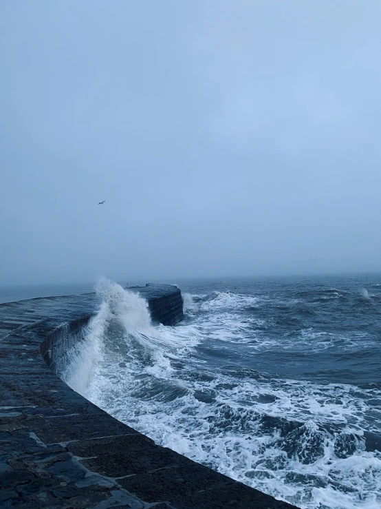 large waves crash into a seawall on a cloudy day