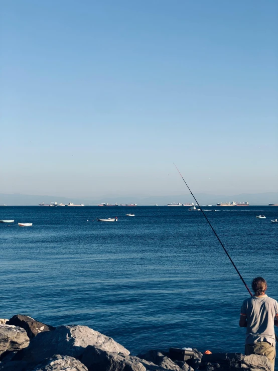 a man fishing while standing on rocks by the water