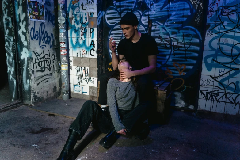 man sitting on womans lap in front of a wall covered with graffiti