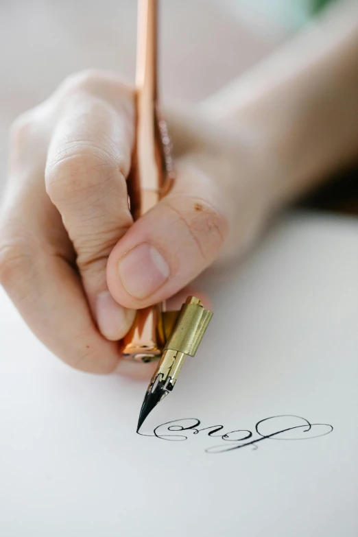 person holding golden pen writing on paper with handwriting