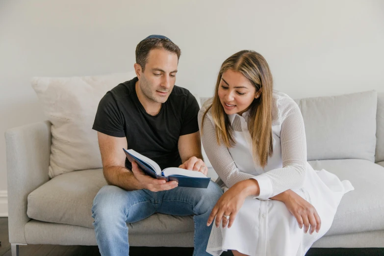 the man and woman are sitting on the couch with an open book