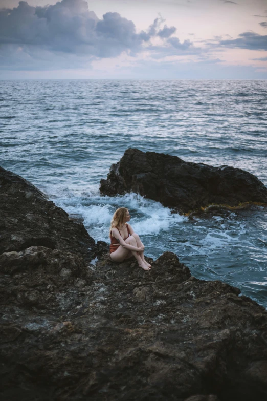 a woman is sitting on the rocks looking out into the water