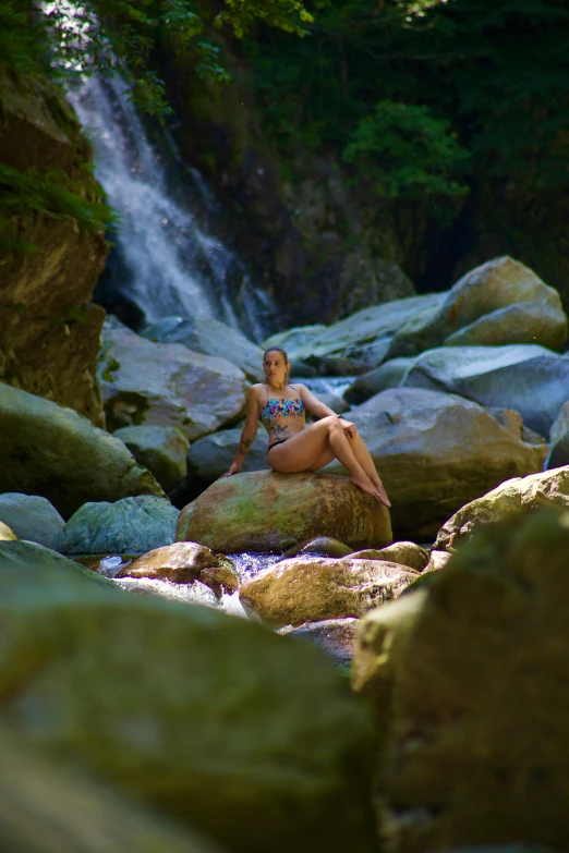 a woman is laying on top of the rocks near the waterfall