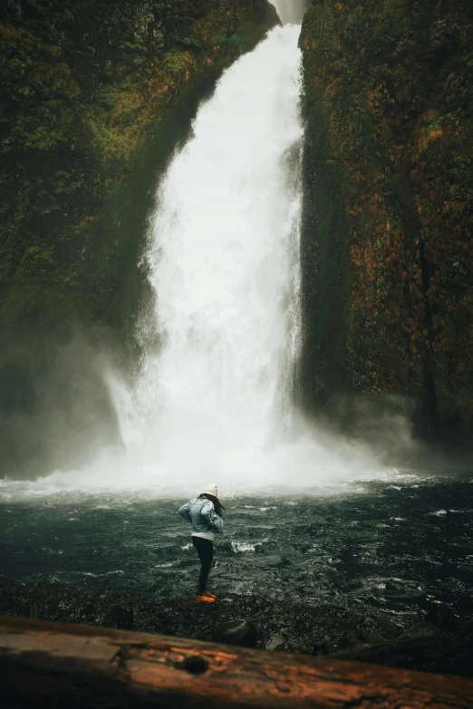 man standing next to waterfall holding an umbrella