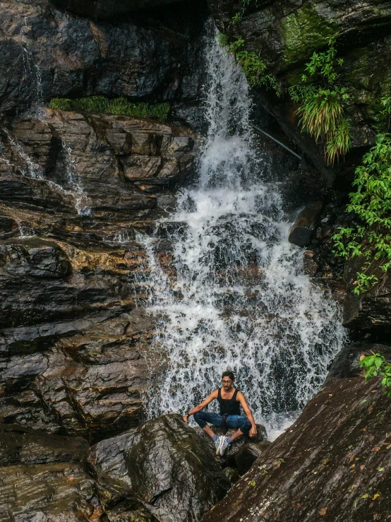 a person sitting on a rock below a waterfall