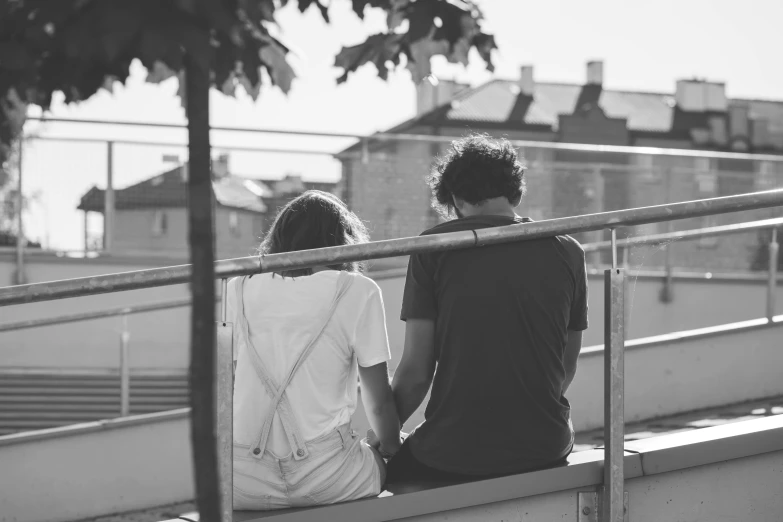 a man and woman sitting on the side of a rail